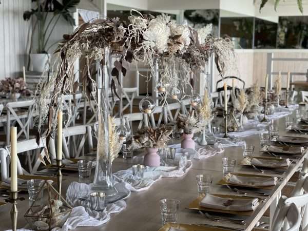 Tablearch, large centrepiece. stunning flower arrangement long table. tall long table florals. hanging lights. cheesecloth runner. draping statement florals