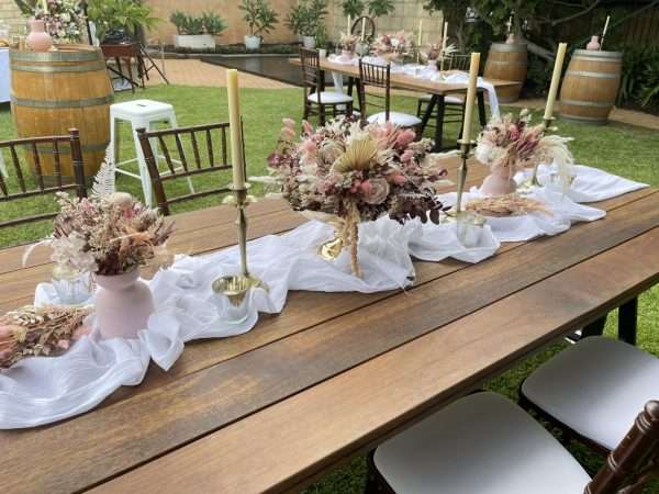 Hire reception table flowers. pink and gold wedding flowers. white cheesecloth wedding table runner. wedding reception long table centrepiece.
