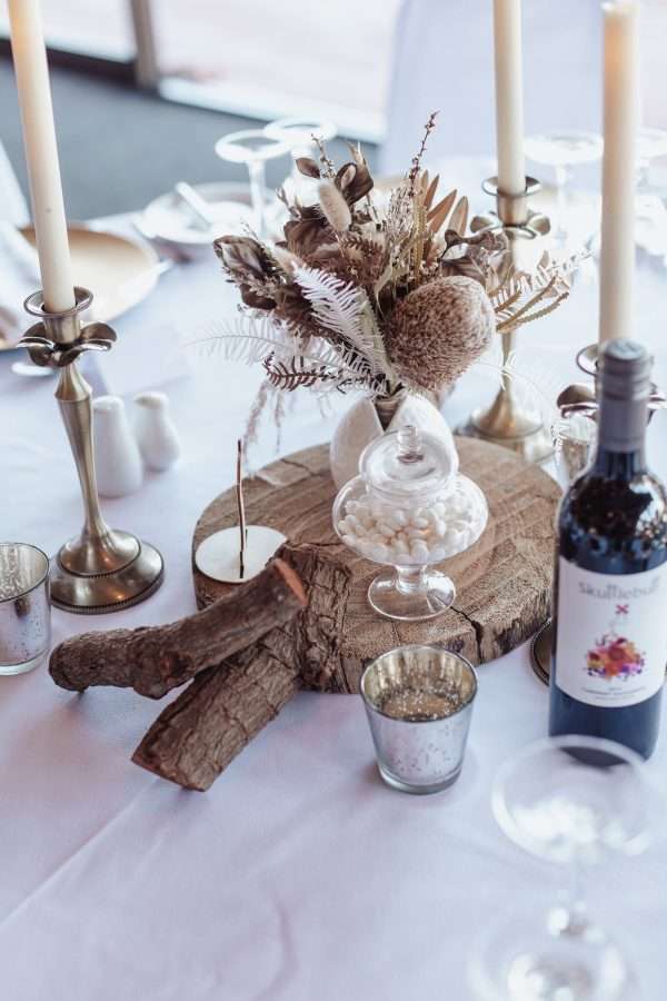 Table centrepiece small rustic look, wood slice and logs, small dried and preserved flower posy in white vase. candlestick